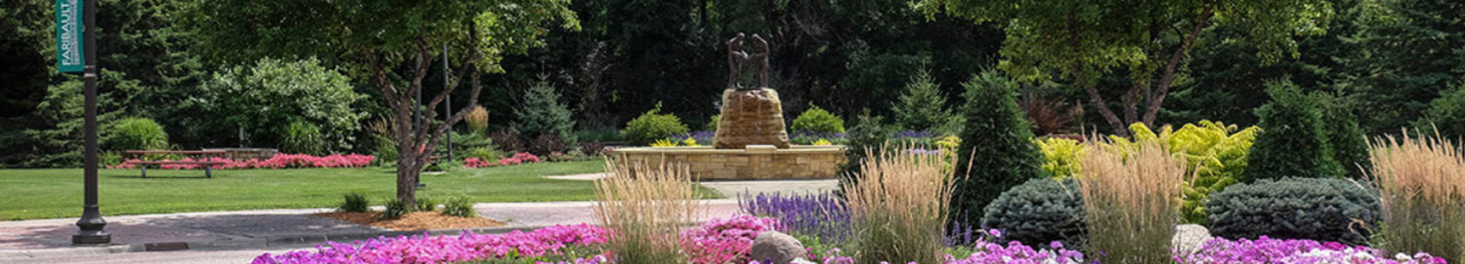 a park with a water fountain, flowers, and trees 